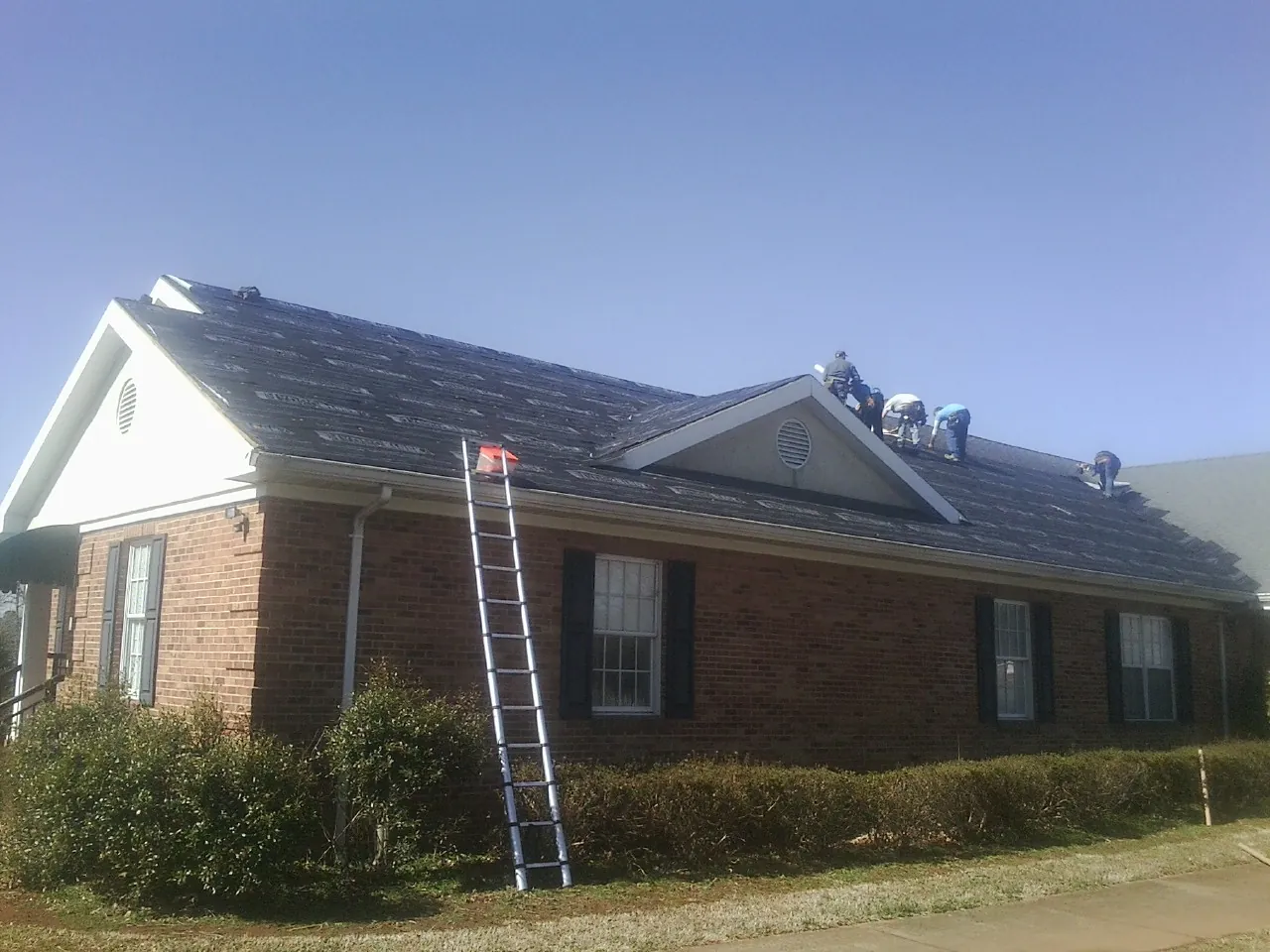 Crew tearing shingles off a brick ranch roof with a ladder set — Emergency Roof Repair work by our crew in Stone Harbor
