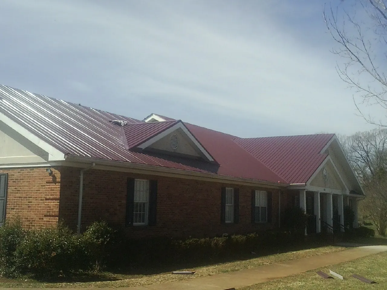 Red metal roof with gabled entries on a long brick building, from a Hail Damage Roof Repair job in Stone Harbor