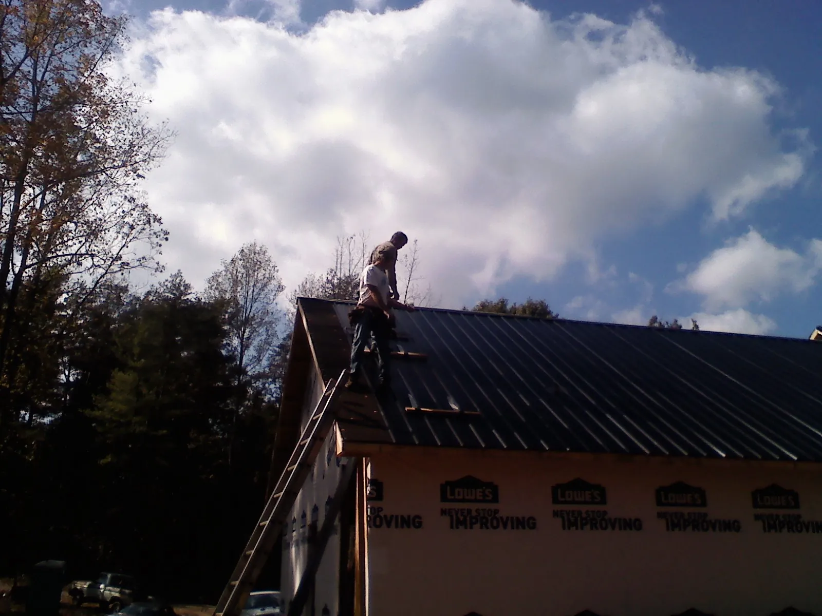 Roofer fastening dark metal panels high against a cloudy sky, from a Roof Inspection job in Stone Harbor